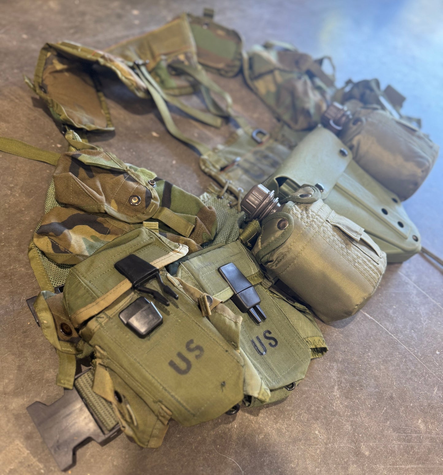 Camouflage tactical vest with various pouches on a concrete floor
