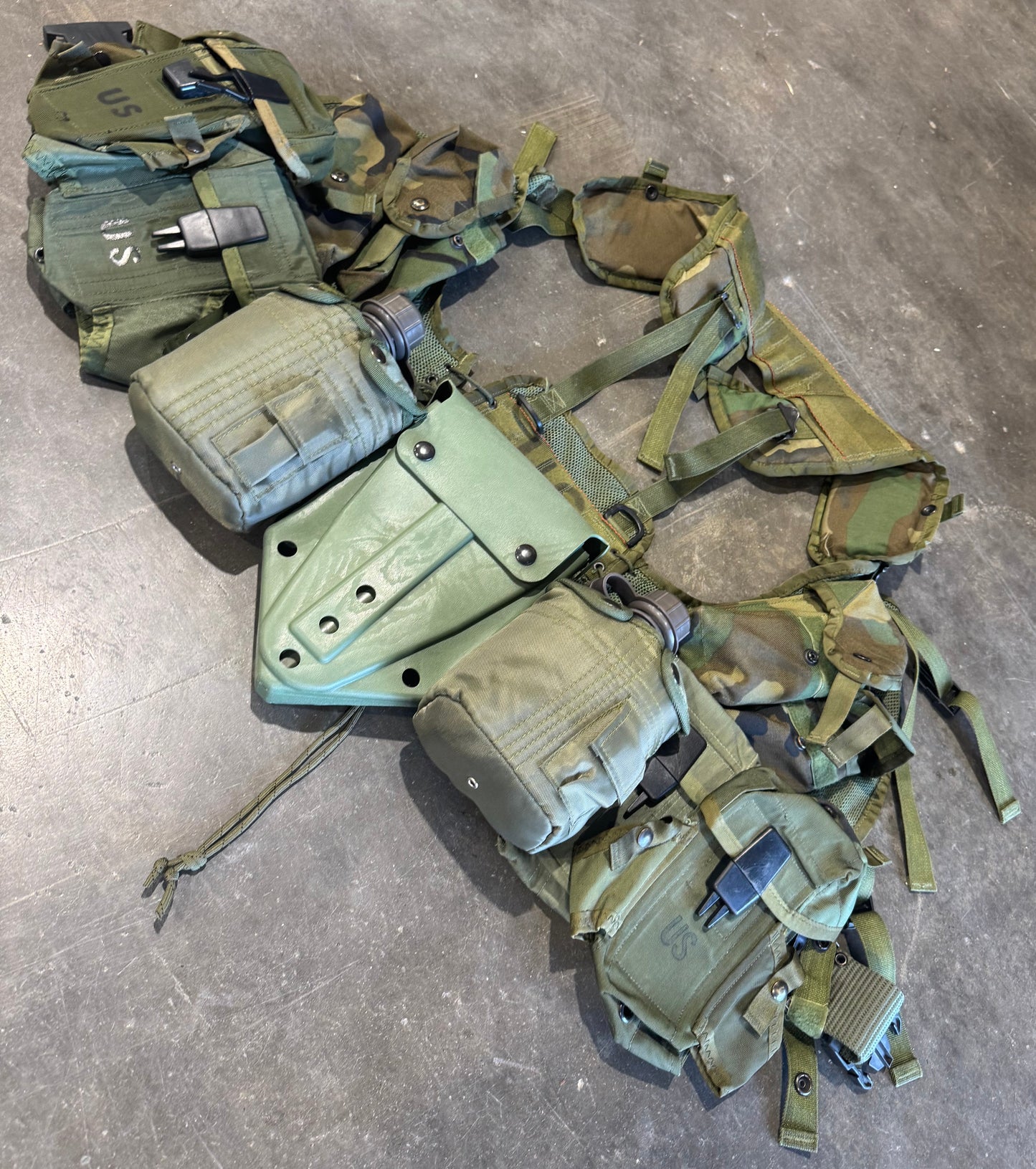 Green tactical vest with multiple pouches on a concrete floor