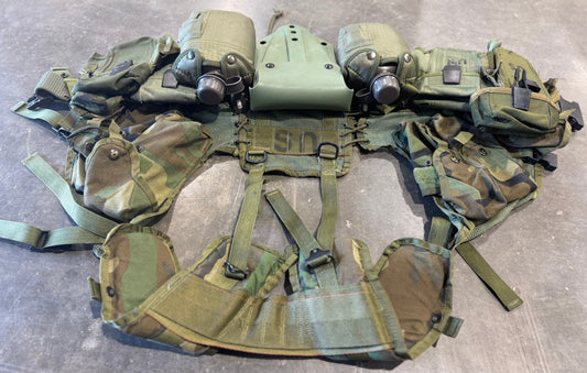 Green tactical vest with multiple pouches and equipment on a gray surface