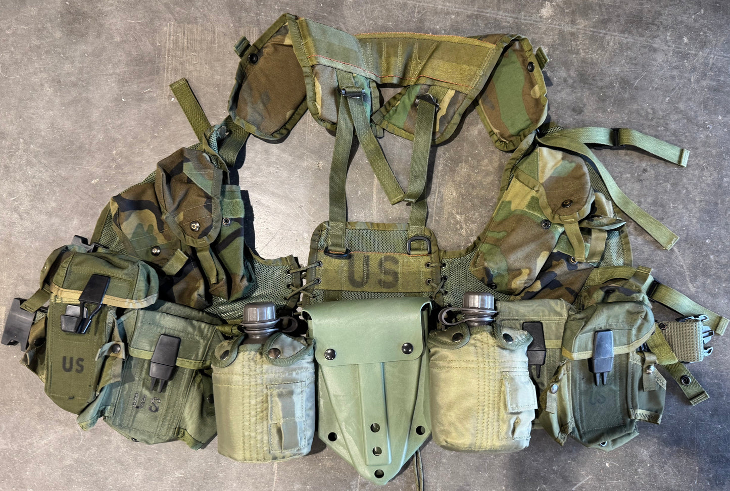 Green tactical vest with multiple pouches on a concrete floor