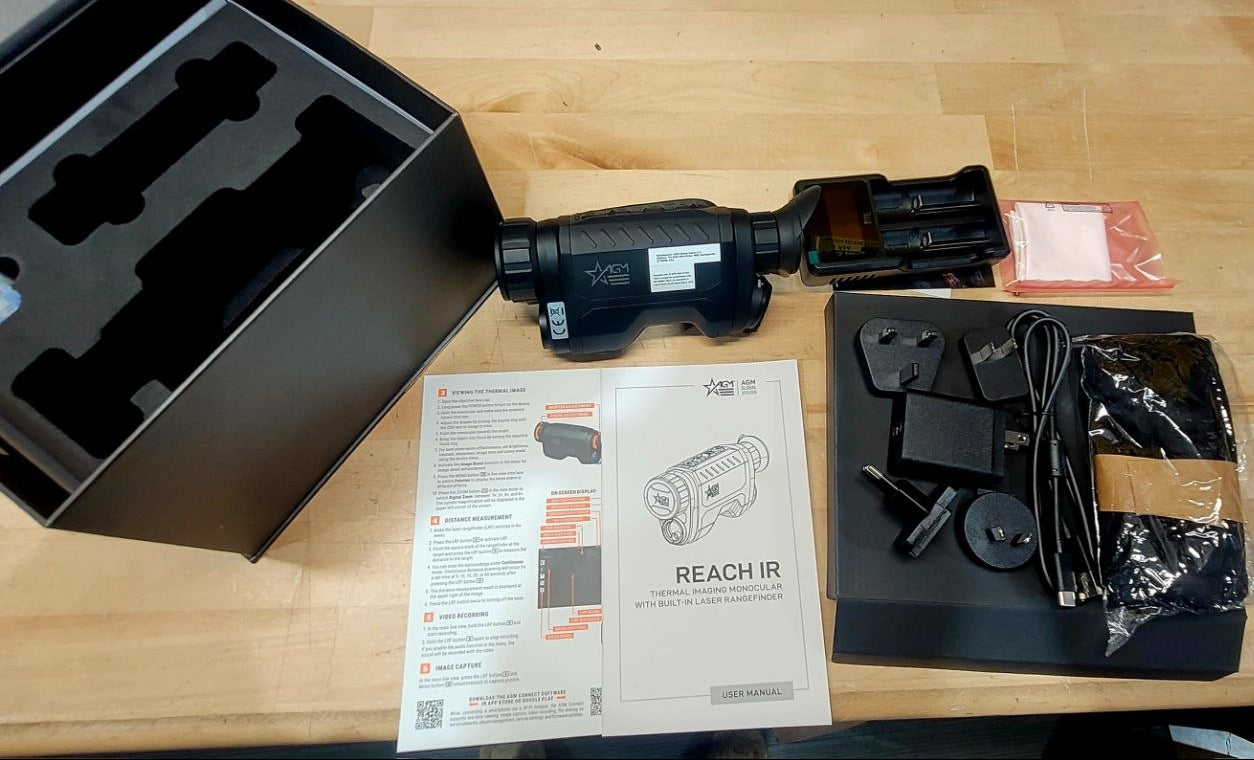 Unboxed thermal imaging camera with accessories and manual on a wooden table