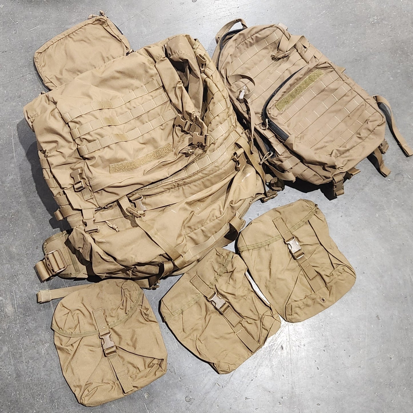 Tan military-style backpack and pouches on a gray concrete floor.