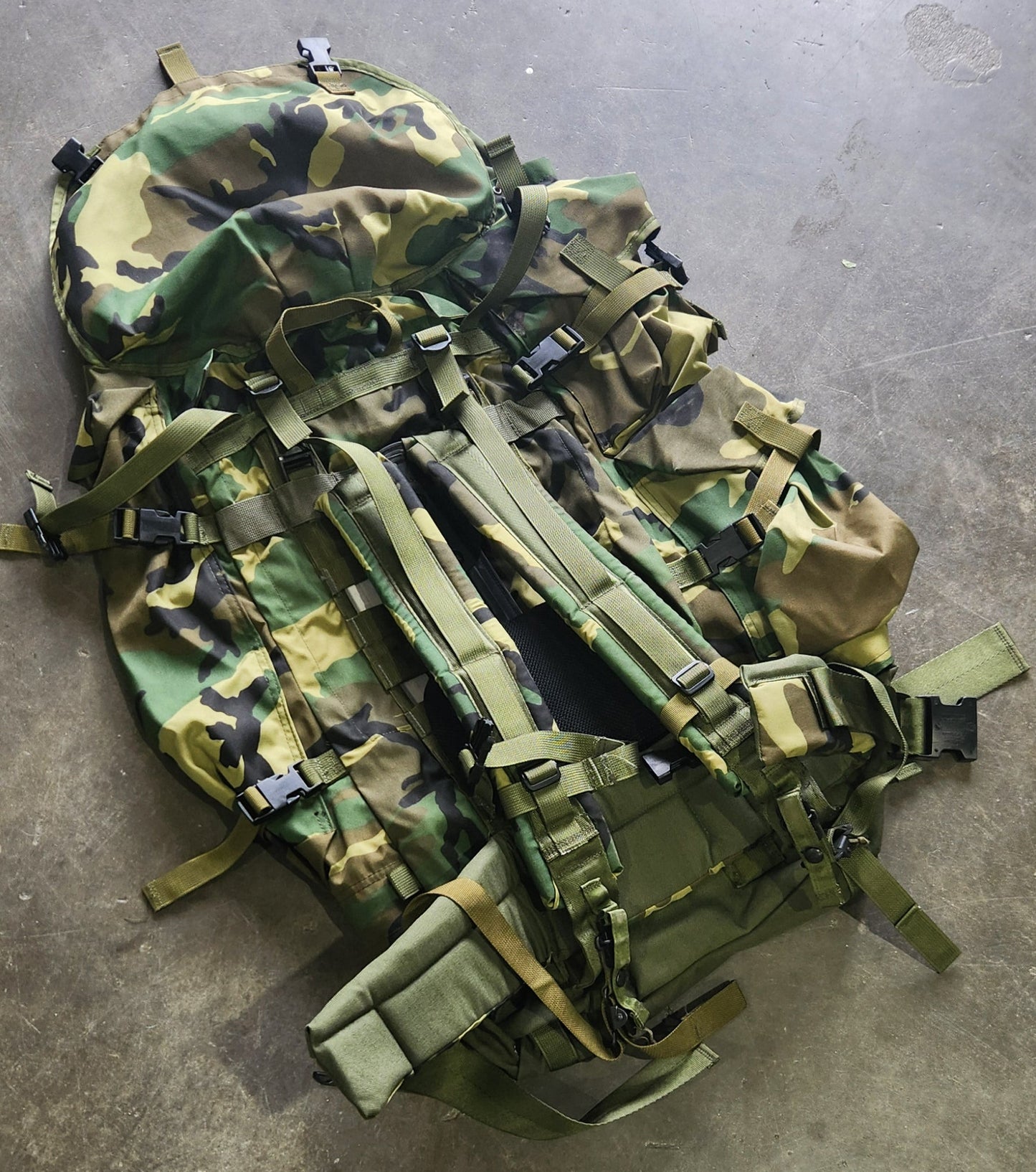 Camouflage backpack on a concrete floor with shoes and a cat in the foreground
