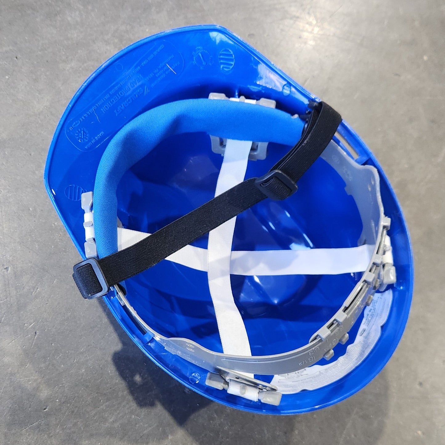 Blue hard hat with a white interior on a gray concrete floor