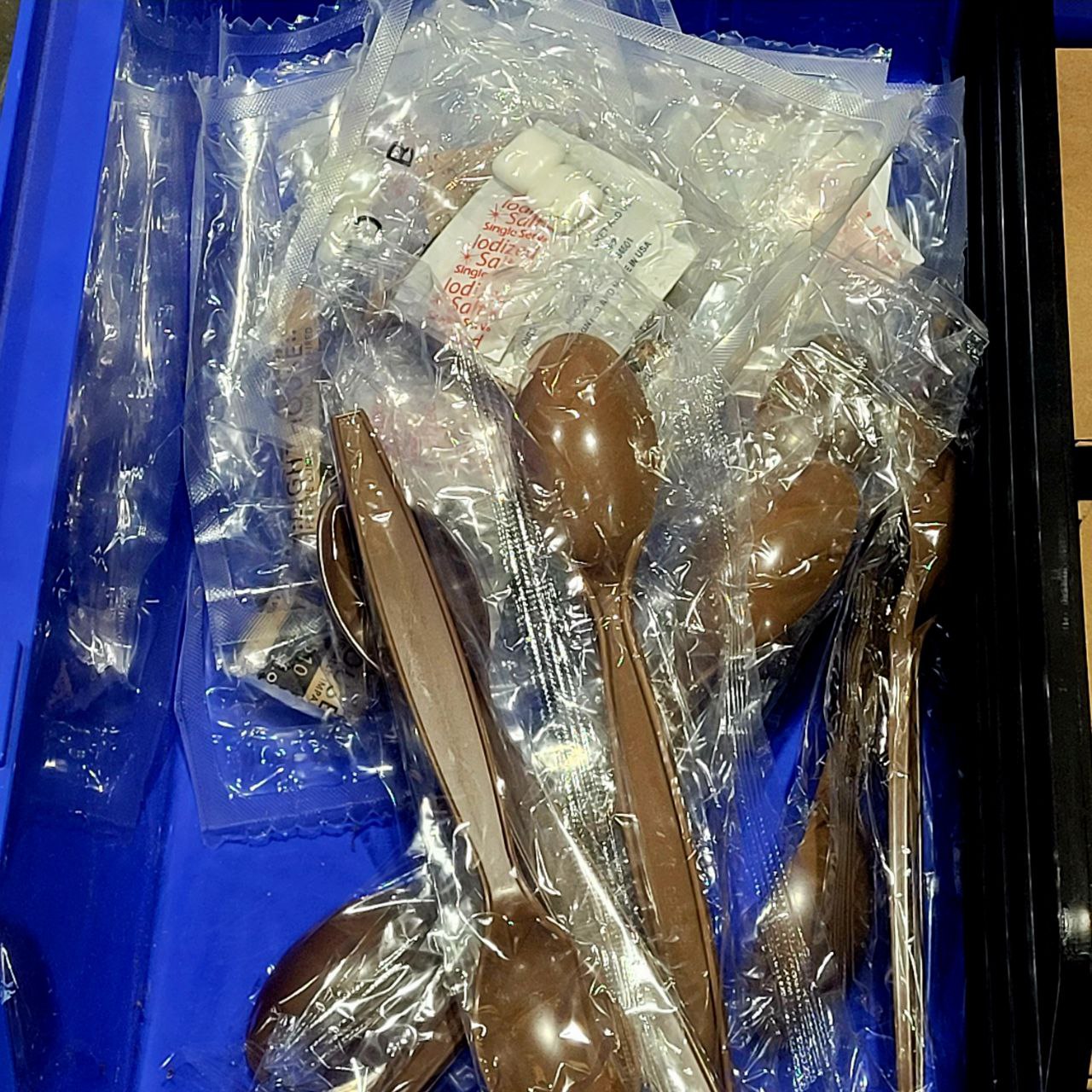 Brown plastic spoons in clear plastic packaging on a blue surface