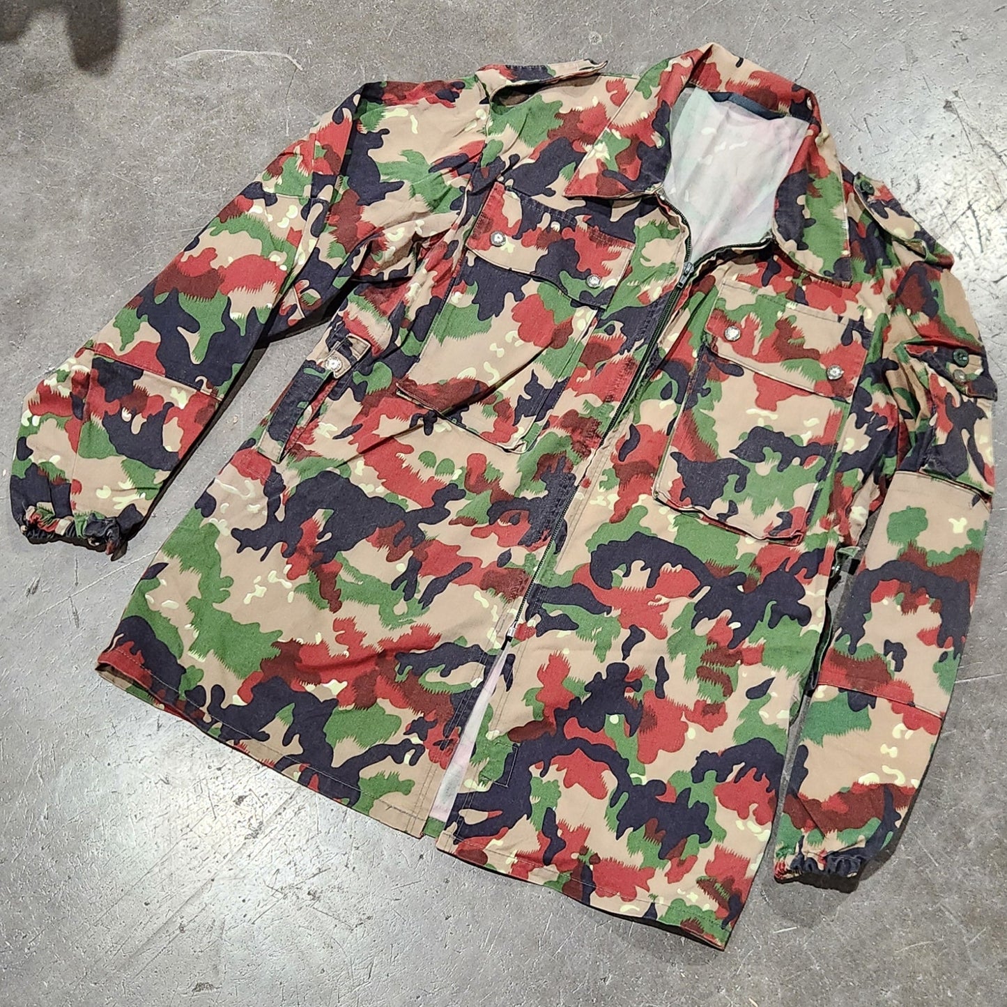 Camouflage-patterned jacket on a concrete floor with shoes and greenery in the background