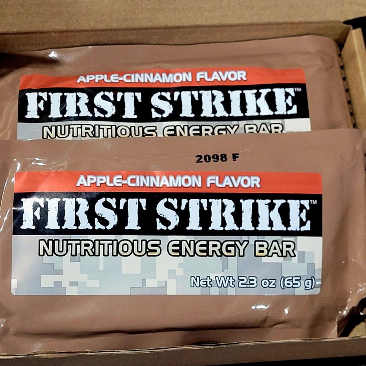 Two 'First Strike' nutritious energy bars in a box, with apple-cinnamon flavor packaging.