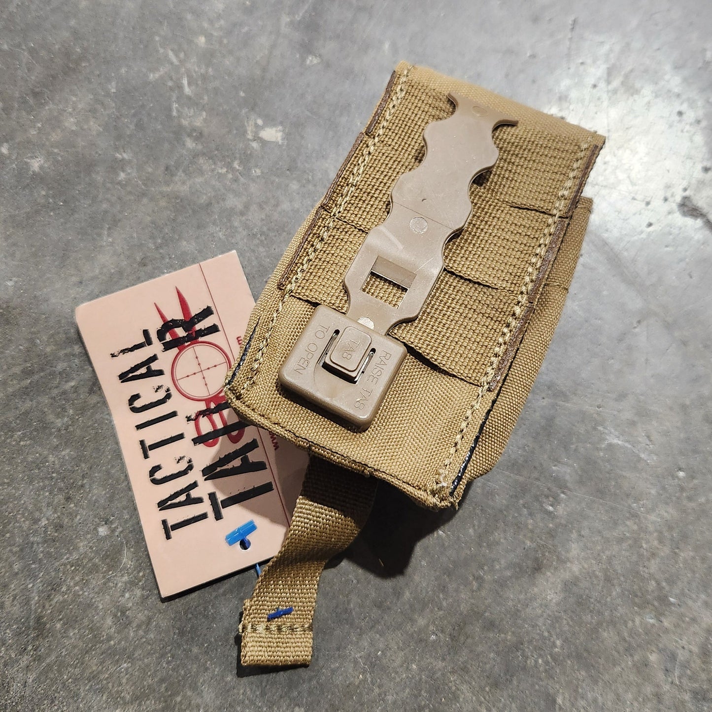 Tan tactical pouch on a metallic surface with a label underneath