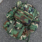 A camouflage patterned rucksack with multiple attachments and straps laid out on the ground.
