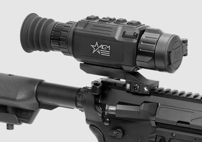 A close-up of a black AGM Optics thermal rifle scope mounted on a black firearm, shown against a light gray background.