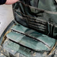 Green tactical bag with multiple compartments on a concrete floor.