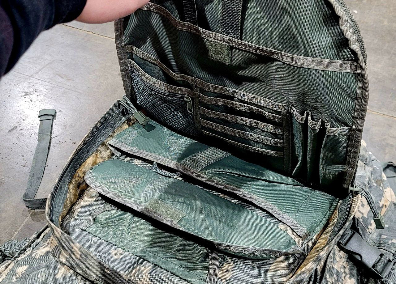 Green tactical bag with multiple compartments on a concrete floor.