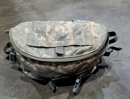 A digital camouflage utility pouch bag with a front flap pocket, resting on a dark gray concrete floor.