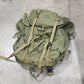 Green backpack on a concrete floor with a person's foot in the background