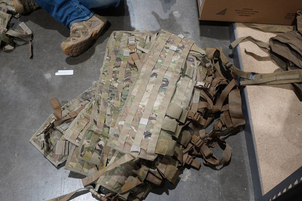 A pile of chest rigs with someone's foot in a boot