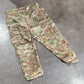 Camouflage pants on a concrete floor with cardboard boxes and shoes in the background