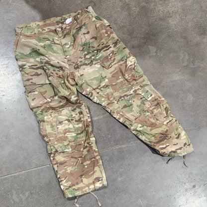Camouflage pants on a concrete floor with cardboard boxes and shoes in the background