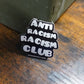 Anti Racism Racism Club sticker on a wooden surface with a metal box in the background