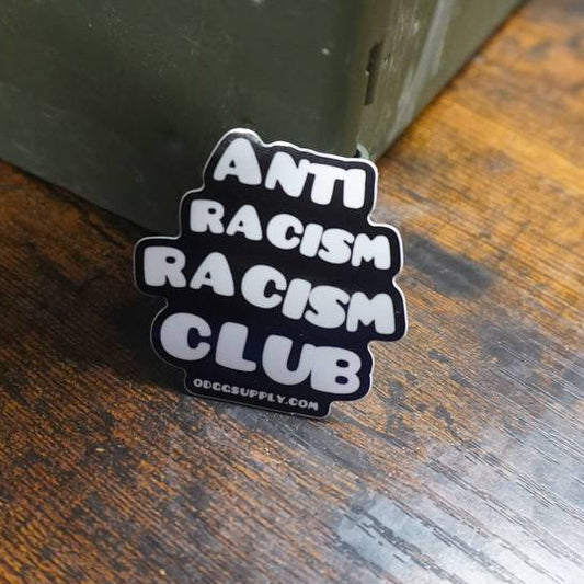 Anti Racism Racism Club sticker on a wooden surface with a metal box in the background