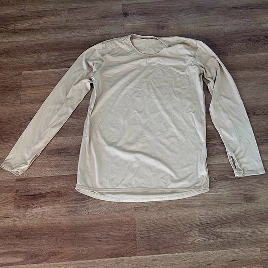 A light beige long-sleeve crewneck shirt laid flat on a brown wood floor.