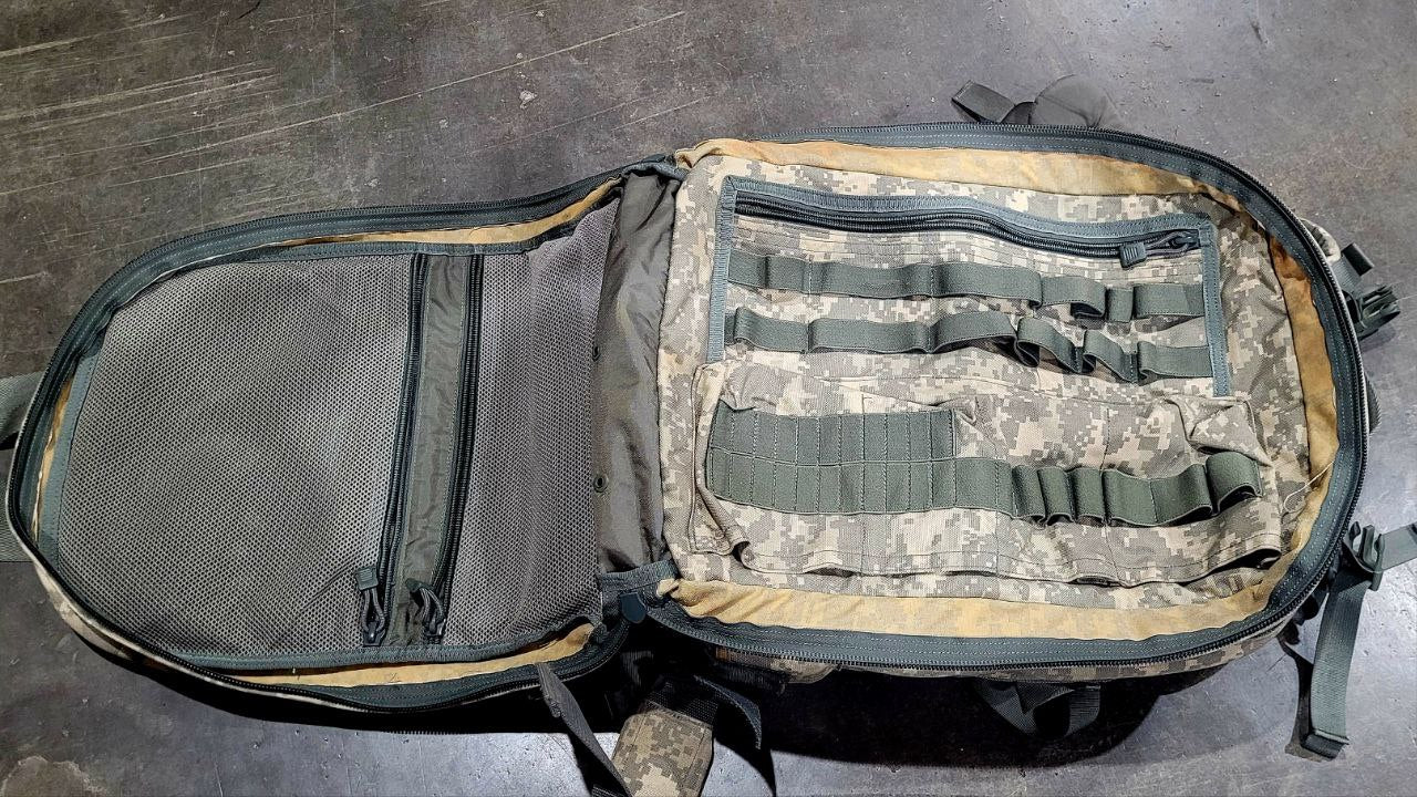 Camouflage backpack with multiple straps on a gray surface