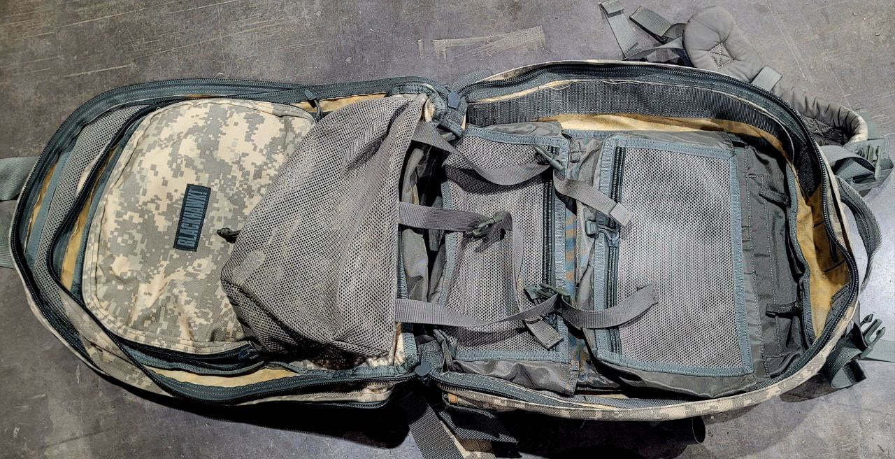 Open tactical backpack with camouflage pattern on a concrete floor