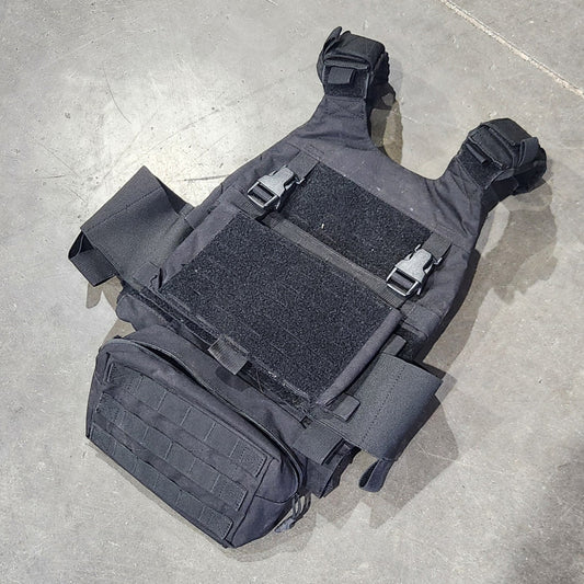 Black tactical vest on a concrete floor with a person's foot partially visible.