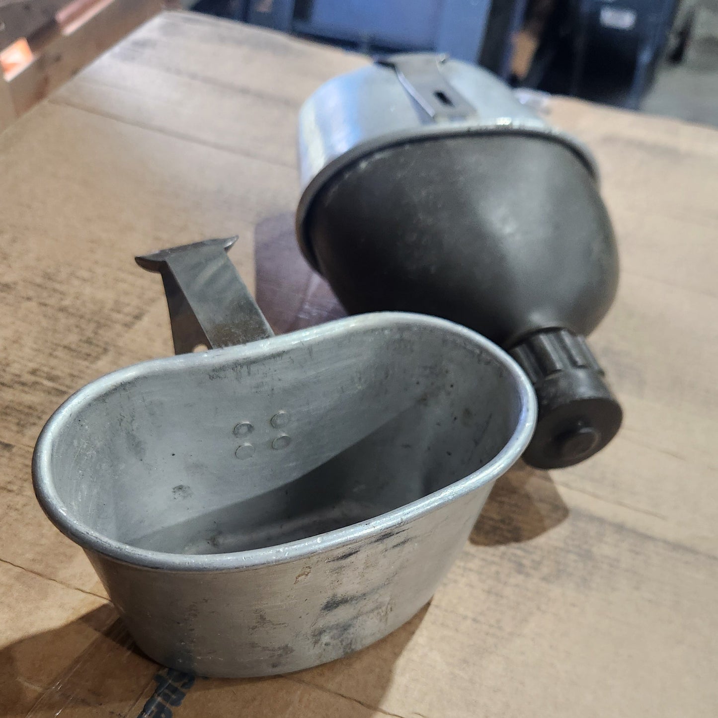 Two vintage metal coffee carafes, one galvanized aluminum and one dark steel, resting on a wooden workbench.