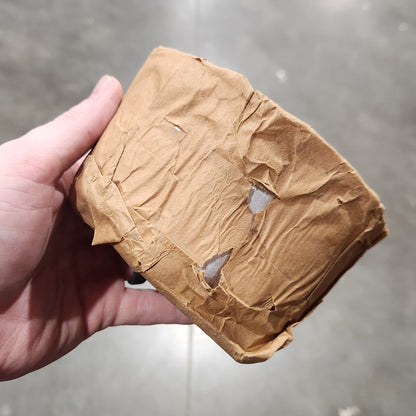 A hand holding a crumpled brown paper bag against a gray concrete floor background.
