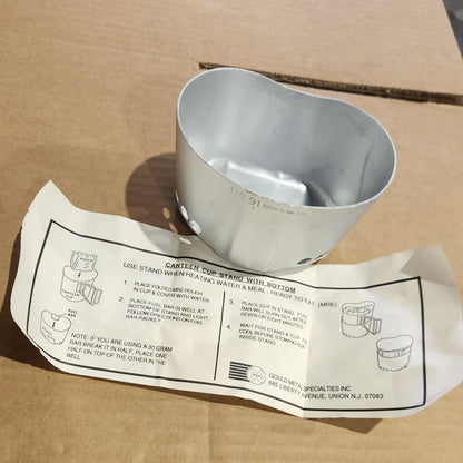 A silver metal elbow pipe fitting placed next to its white paper instruction sheet on a brown cardboard surface.