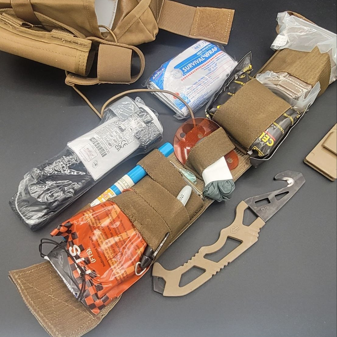  tactical gear including a knife, pouches, and supplies on a gray surface