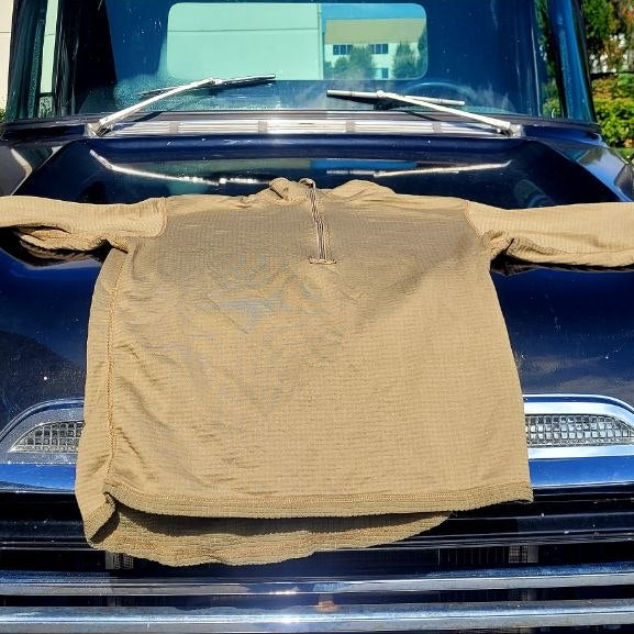 A tan long-sleeve shirt is draped across the front of a dark blue vintage car outdoors.