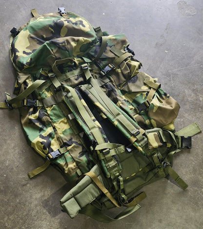 Camouflage backpack on a concrete floor with shoes and a cat in the foreground