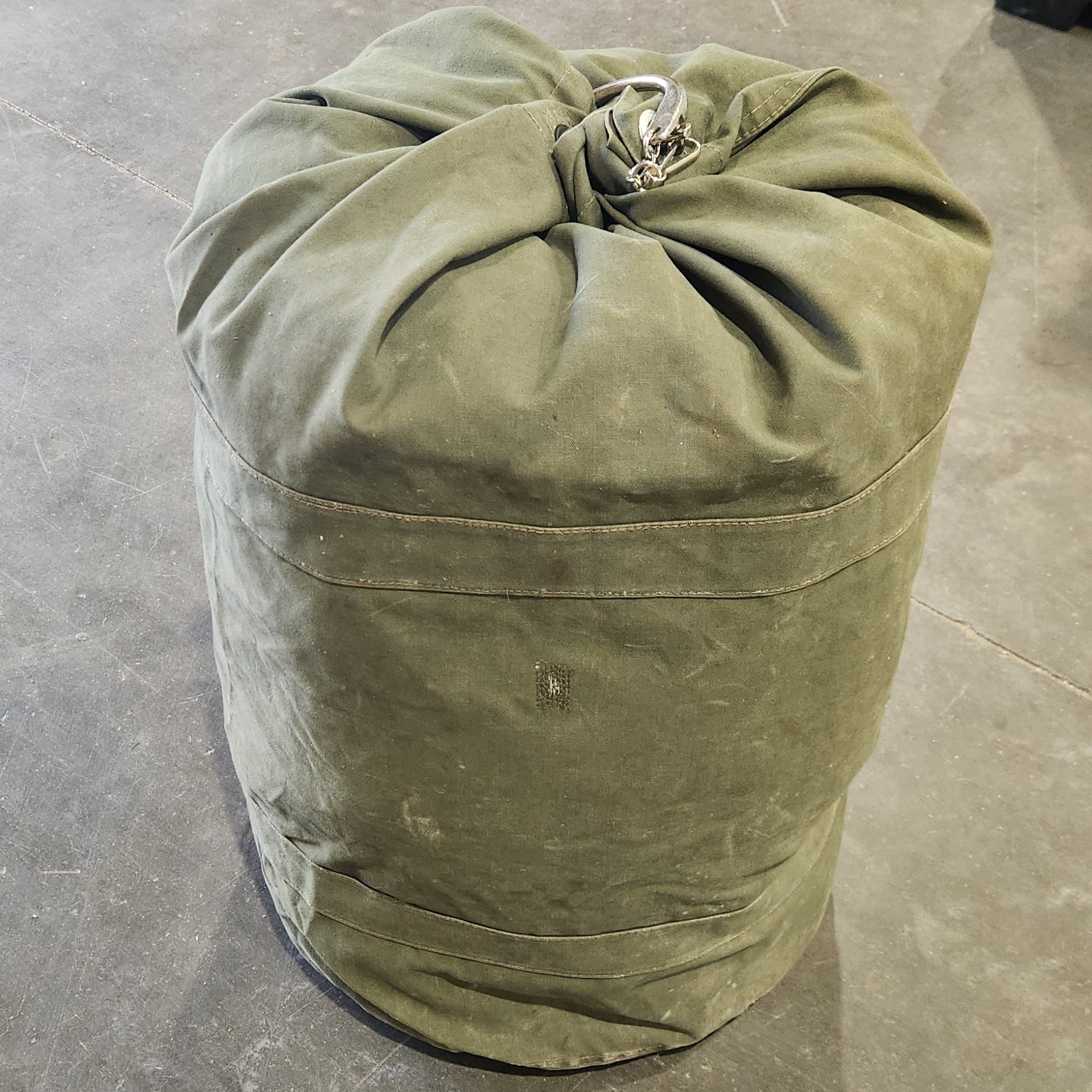 Green duffel bag rolled up on a concrete floor