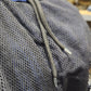 Close-up of a dark gray mesh pocket with a drawstring closure on a blue bag, showing the texture of the mesh material.