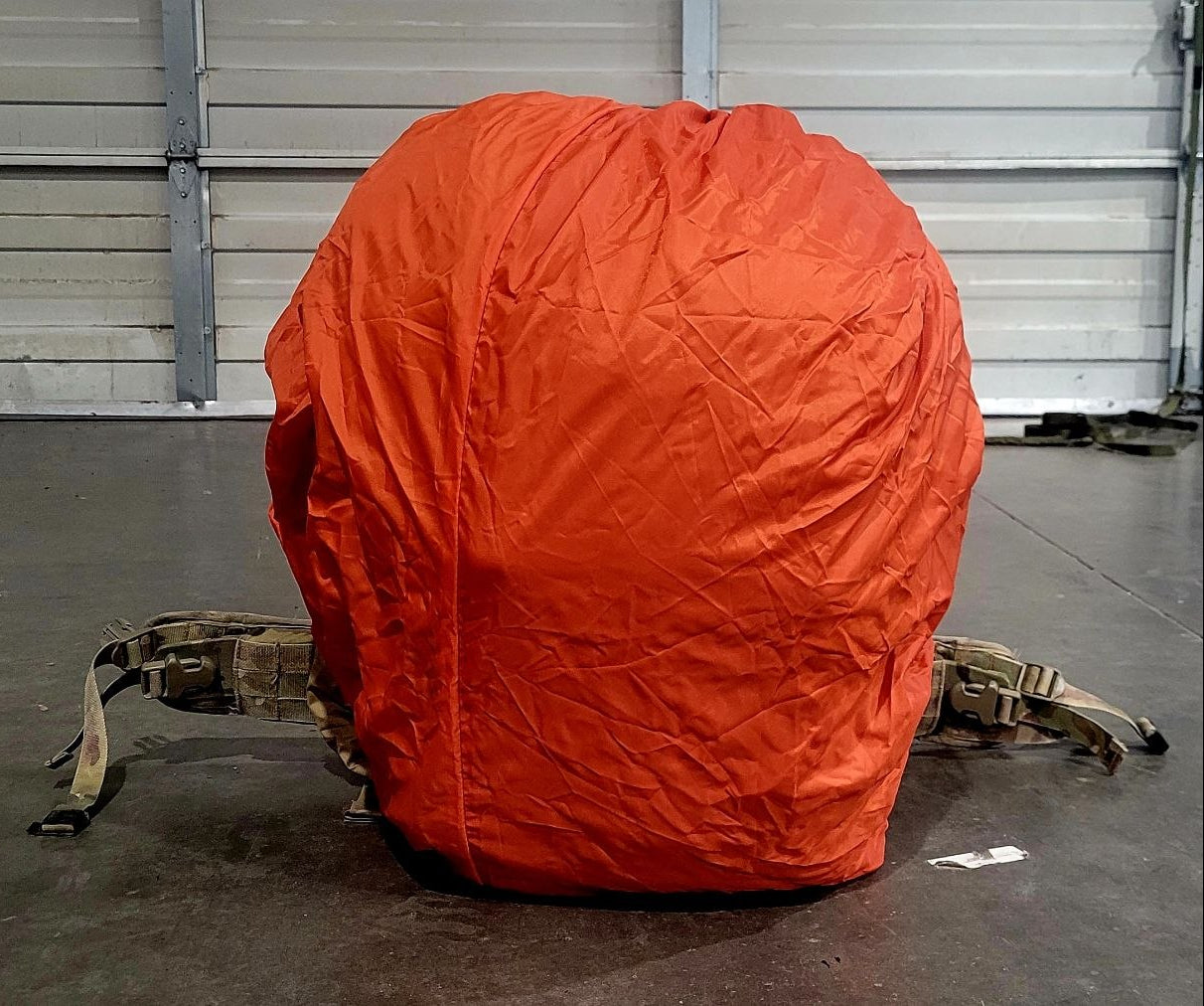 Orange vehicle cover on a rucksack in front of a metal garage door.
