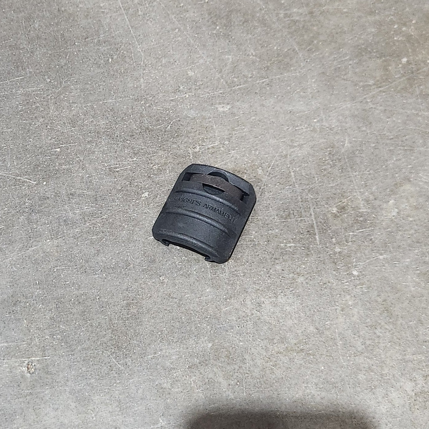 Several black cylindrical grip-like accessories are scattered on a gray concrete floor, with one held in a hand in the lower right corner. A cardboard box edge is visible on the left.