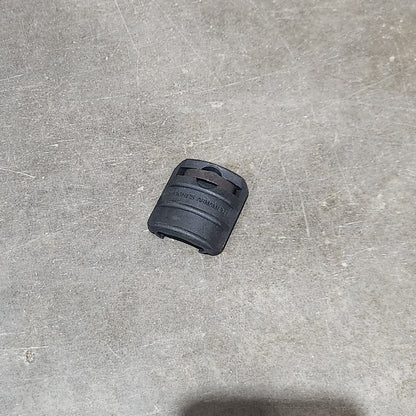 Several black cylindrical grip-like accessories are scattered on a gray concrete floor, with one held in a hand in the lower right corner. A cardboard box edge is visible on the left.