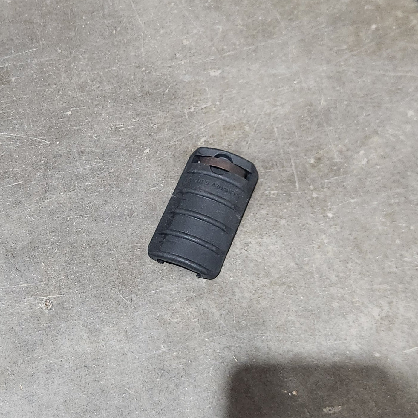 Several black cylindrical textured grip or sleeve components scattered on a concrete floor, with a cardboard box edge visible at the left.