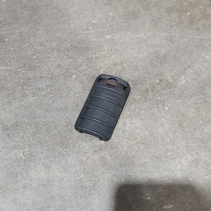 Several black cylindrical textured grip or sleeve components scattered on a concrete floor, with a cardboard box edge visible at the left.