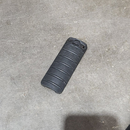 Several black textured cylindrical grip or handle components arranged on a gray concrete floor next to a cardboard box.