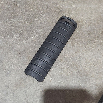 Several black textured cylindrical foam or rubber grips are scattered on a concrete floor, with a cardboard box edge visible on the left and a large shadow across the upper right area.