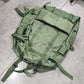 Green military-style backpack on a concrete floor with a cardboard box nearby.