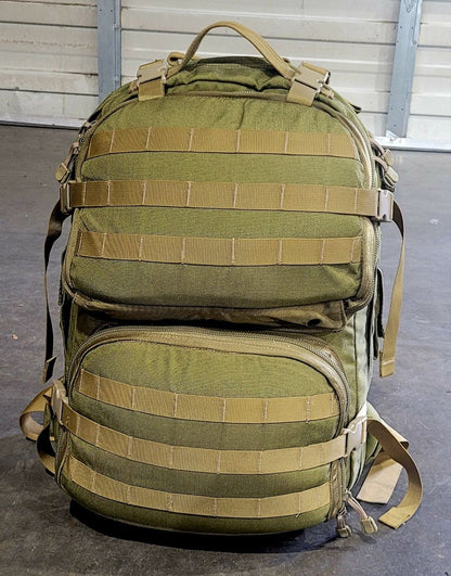 Green tactical backpack with multiple straps on a gray floor.