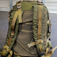 Green tactical backpack with multiple straps on a gray floor.
