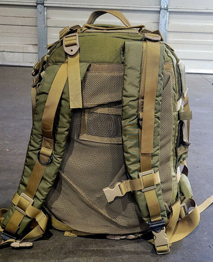 Green tactical backpack with multiple straps on a gray floor.