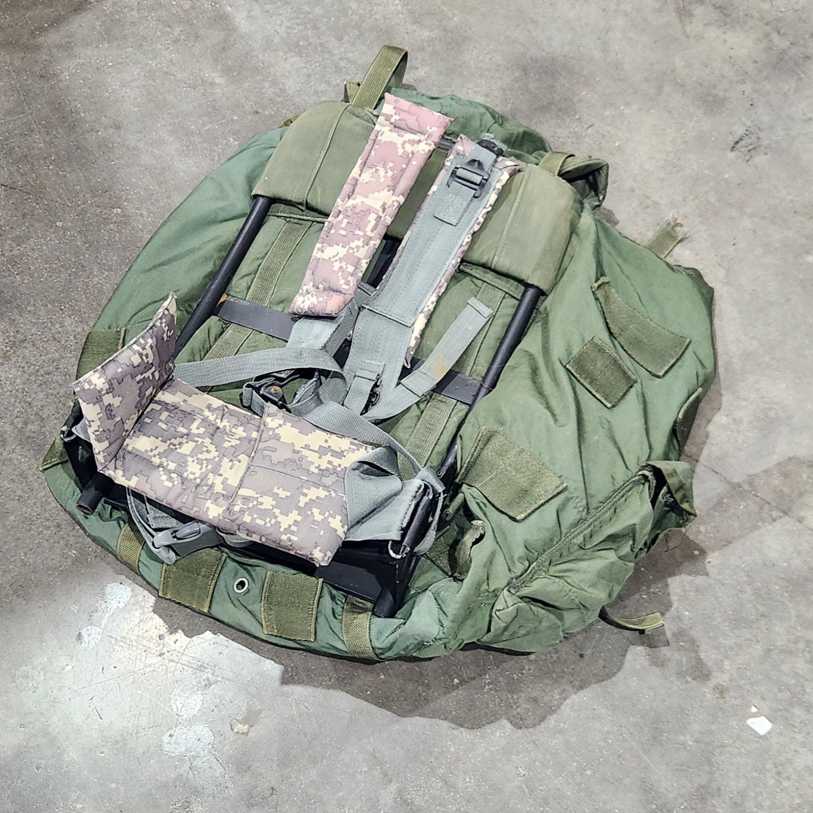 Green military-style backpack on a concrete floor