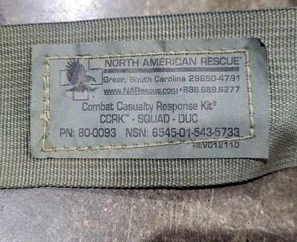 Close-up of a sewn fabric label reading NORTH AMERICAN RESCUE with contact information and Combat Casualty Response Kit text, attached to olive drab fabric.