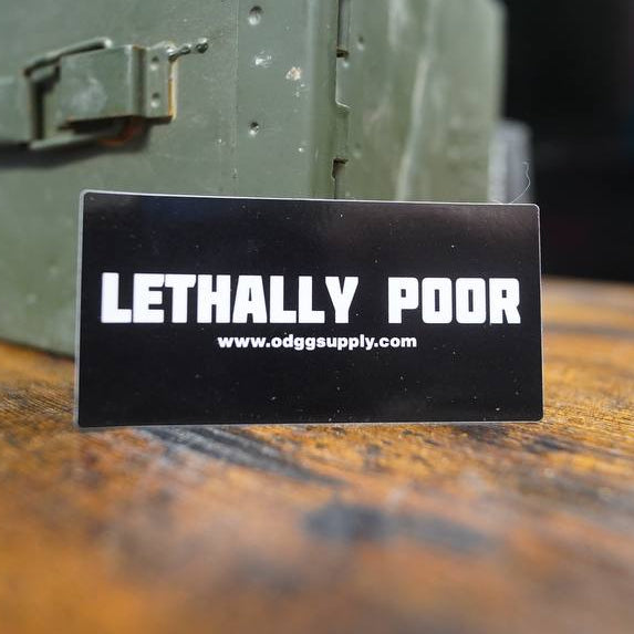 Card with 'Lethally Poor' branding on a wooden surface with a metal box in the background.