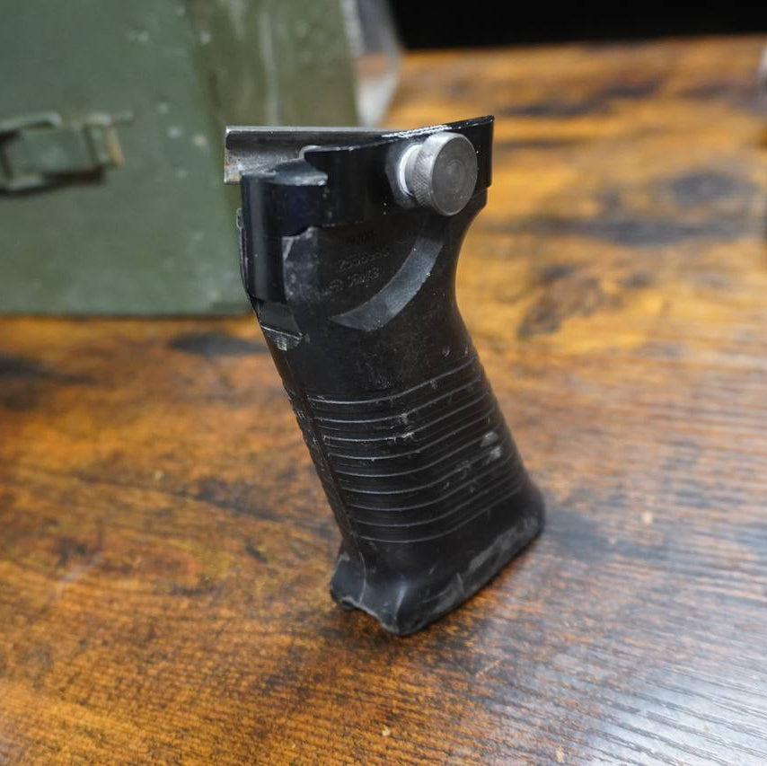 Black gun grip on a wooden surface with a green box in the background